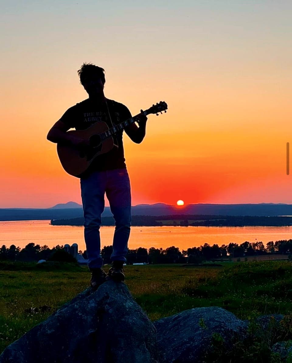 Silhouette de Nate Couture, guitare à la main, au coucher du soleil